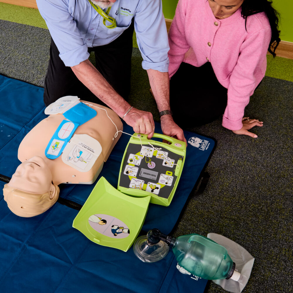 Image of one of our trainers of the Basic Life Support training course demonstrating a defibrillator to an attendee.
